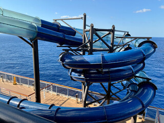Curved blue and clear transparent tube slide spiraling down the side of a modern cruise ship,...
