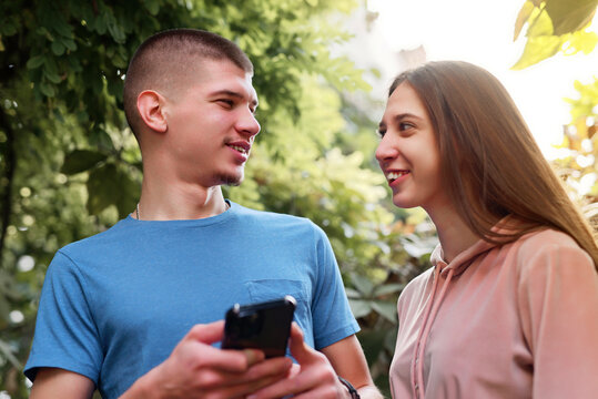 Young couple enjoys conversation in a lush garden during a sunny afternoon while using a smartphone