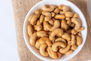 Top view piles of roasted tasty cashews in a white bowl on natural background