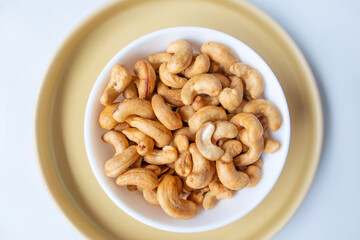 Top view piles of roasted tasty cashews in a white bowl on yellow background