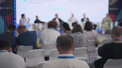 Audience members sit attentively during a professional seminar with panel discussion taking place.