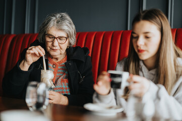 An elderly woman stirring her drink while a young girl is sitting next to her in a cafe booth, symbolizing family bonding and inter generational connection.