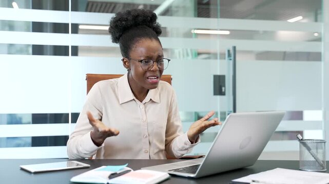 Angry african american businesswoman arguing talking on a video call on a laptop computer at workplace in business office. Frustrated black woman boss emotionally talks with subordinate about problems