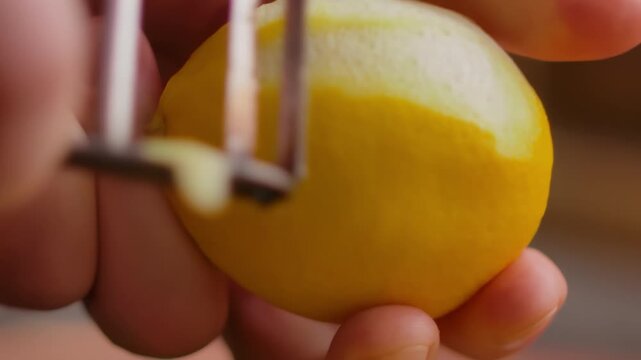 Macro view of a zester knife peeling a thin spiral from a lemon. This aromatic zest is a key ingredient for the Italian condiment gremolata. Concept of gourmet cooking and fresh flavor