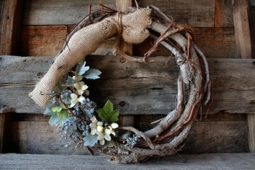 Rustic wreath adorned with greenery and flowers hanging against wooden background