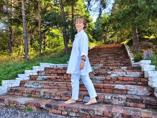 Middle-aged woman enjoying a barefoot walk on steps in a lush setting during her travel adventure