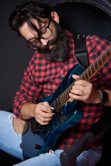 Bearded man playing guitar in a studio setting with relaxed atmosphere and creative vibes