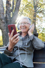 Senior woman enjoying music while sitting on a park bench during a sunny autumn day