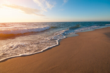 Sandy beach and sea waves by sunset