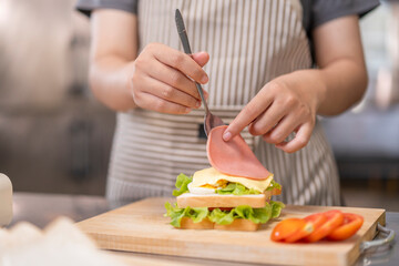 Hand using a spoon to add ham on a sandwich.