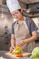 A young Asian woman placing slice of cheese on homemade sandwich.