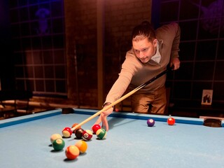 Fototapeta premium Brunette middle-age man holding arm on billiard table, playing snooker game or preparing aiming to shoot pool balls. sport game snooker billiards