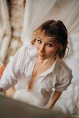 Naklejka premium sexy woman in white shirt in bed by window. female attractiveness and sexuality.