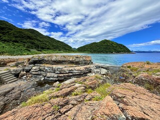 Aerial drone view of Senjojiki on Naru Island, Goto Islands, Nagasaki, Japan – coastal rock terraces, turquoise waters, and lush green landscape under clear summer sky.
