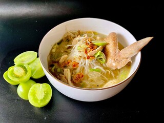Soto ayam, a typical Indonesian dish, is served in a white bowl with an isolated black background