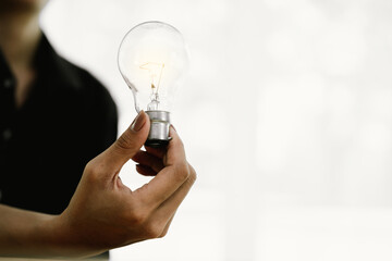 A person holds a glowing light bulb over stacked coins, symbolizing creativity, financial growth,...
