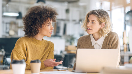 Two professional women are engaged in a serious business conversation while working together at a shared desk. They are looking at each other. Concept of teamwork, communication, office life