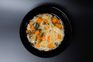 Vermicelli soup with carrots, potatoes and greens in a black bowl isolated on a black background