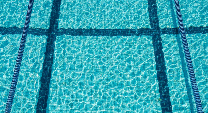 Overhead view of turquoise swimming pool water texture, showing lane lines and ripples, creating a refreshing and dynamic appearance, ideal for summer or aquatic themes