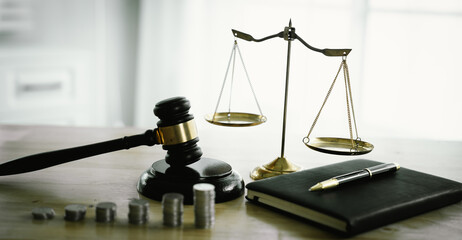 A gavel rests beside stacked coins and a balance scale, symbolizing justice, legal decisions,...