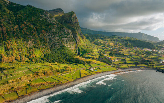 Aerial view of dramatic cliffs meeting the ocean near Po&Atilde;&sect;o do Bacalhau, as terraced fields cascade down to the Faj&Atilde;&pound; Grande coastline, Faj&Atilde;&pound; Grande, Azores, Portugal.