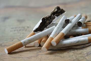 Pile of cigarettes, some broken, lies on old map, symbolizing global impact of smoking. image highlights health risks and environmental concerns associated with tobacco use