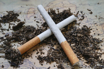 Two cigarettes crossed on map background surrounded by loose tobacco, creating rustic and contemplative atmosphere. image suggests themes of travel and habit