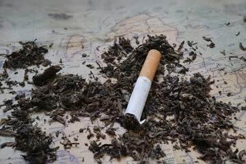 Cigarette lies on vintage map surrounded by scattered tobacco, creating nostalgic and contemplative atmosphere. scene evokes thoughts of travel and passage of time