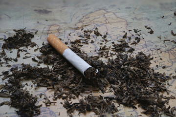 Cigarette lies on vintage map surrounded by scattered tobacco, symbolizing impact of smoking on global health. image evokes sense of urgency and awareness