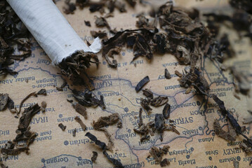 Close up of partially unrolled cigarette with loose tobacco scattered on old map, creating vintage and rustic atmosphere. map text is visible, adding element of exploration