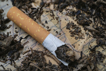Broken cigarette lies on bed of loose tobacco, with its contents spilling out onto vintage paper background, evoking sense of decay and nostalgia