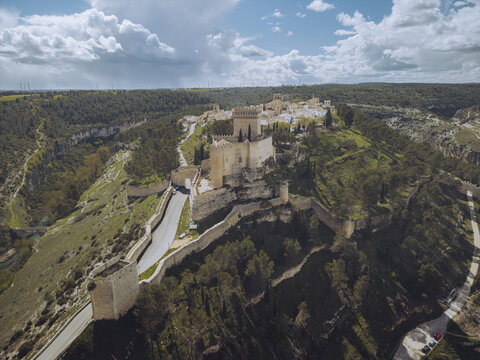 Aerial view of a medieval castle perched atop a rugged cliff, its stone walls bathed in the warm glow of the setting sun, Alarc&Atilde;&sup3;n, Castile-La Mancha, Spain.