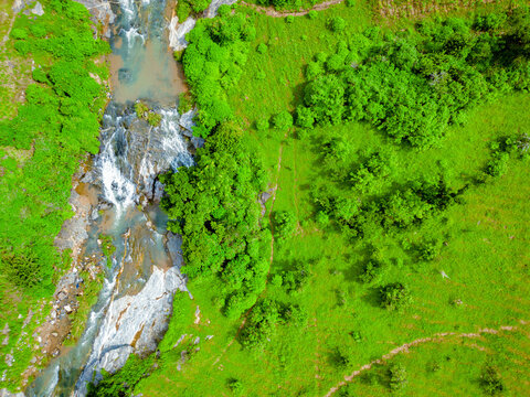 Aerial view of a vibrant green landscape meeting a rocky riverbed, water cascading down, creating a serene meeting of nature's contrasts, Maza village, Jos North, Nigeria.