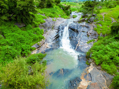 Aerial view of cascading waterfall plunges into a clear pool surrounded by vibrant green vegetation, Maza village, Jos North, Nigeria.