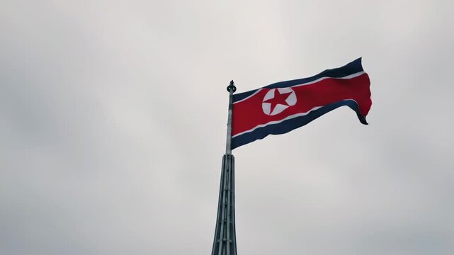 north korea national day. korean flag waving against cloudy sky on tall flagpole. national symbolism and sovereignty. travel, political and cultural identity.