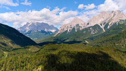 Aerial view of scenic alpine valley with pine forest and rocky mountain range under blue sky on a summer day