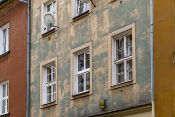 Weathered facade of an old townhouse with visible windows and a satellite dish. Faded green and beige plaster showing signs of age and decay. Close-up of urban residential architecture.
