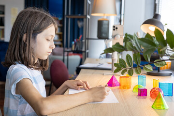 Teen girl studying geometric shapes at school desk, preparing for back to school season and exploring math concepts through colorful 3D figures during interactive learning activity in class.