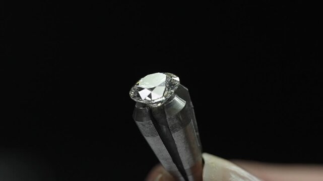 Macro close-up of a sparkling diamond held in a dop stick being rotated for inspection and polishing