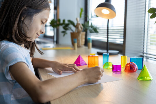 Teen girl studying geometric shapes at school desk, preparing for back to school season and exploring math concepts through colorful 3D figures during interactive learning activity in class.