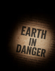 Vintage-styled newspaper close-up with spotlight effect highlighting the phrase 'EARTH IN DANGER', representing environmental urgency.