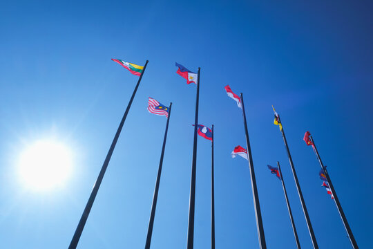 ASEAN member country flags waving on tall poles under bright sunlight blue sky. Southeast Asian unity. International relations and diplomacy.