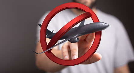 Image depicts a hand holding a model airplane crossed out by a red circle, symbolizing travel...