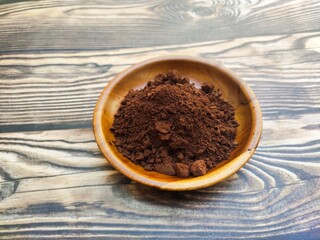 A closeup of a pile of chocolate powder in a wooden dish on a wooden table. Chocolate powder is a powder made from cocoa beans or Theobroma cacao that has been roasted, shelled, and ground.