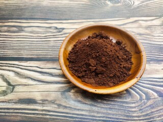 A closeup of a pile of chocolate powder in a wooden dish on a wooden table. Chocolate powder is a powder made from cocoa beans or Theobroma cacao that has been roasted, shelled, and ground.