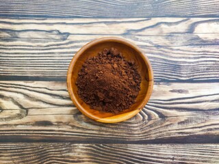 A closeup of a pile of chocolate powder in a wooden dish on a wooden table. Chocolate powder is a powder made from cocoa beans or Theobroma cacao that has been roasted, shelled, and ground.