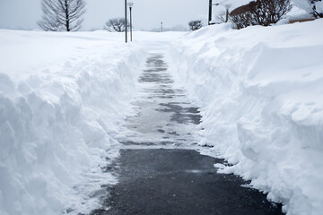 A snowy path cleared after a heavy snowfall, creating a serene winter scene with white and gray hues.