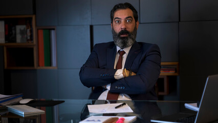 A middle-aged, dark-haired businessman in a suit is experiencing great shock while working at his...