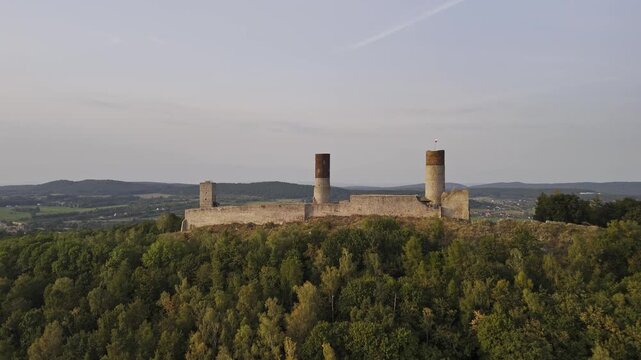 A smooth aerial flyover above Checiny Castle in Poland, showcasing the medieval stone fortress, its towers, and the lush green landscape surrounding it.