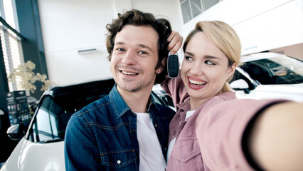 Fototapeta premium Happy couple taking selfie in car showroom, showcasing excitement after purchasing new vehicle, surrounded by modern cars and bright atmosphere